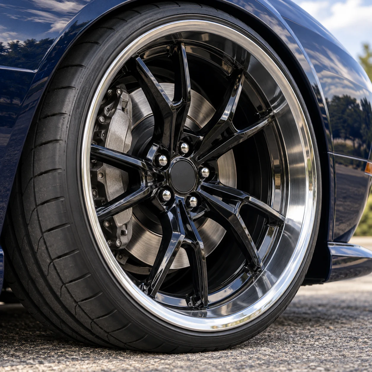 Illustrative close-up of a gloss black split-spoke forged wheel with polished lip and big brake caliper